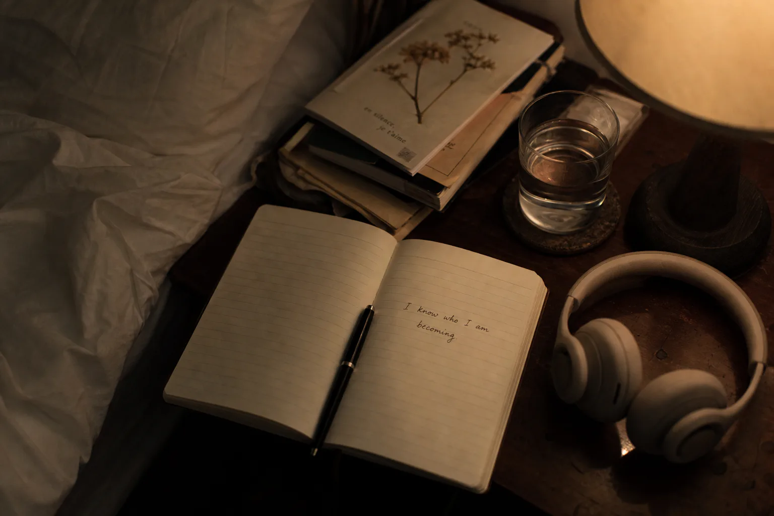 Notebook and headphones beside a dim bedside lamp