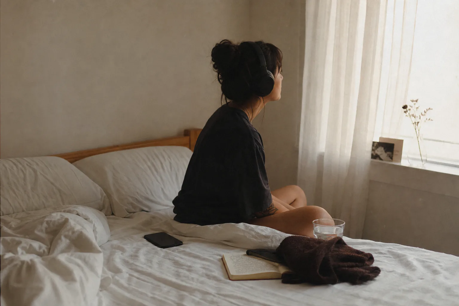 Woman listening to audio beside an unmade bed
