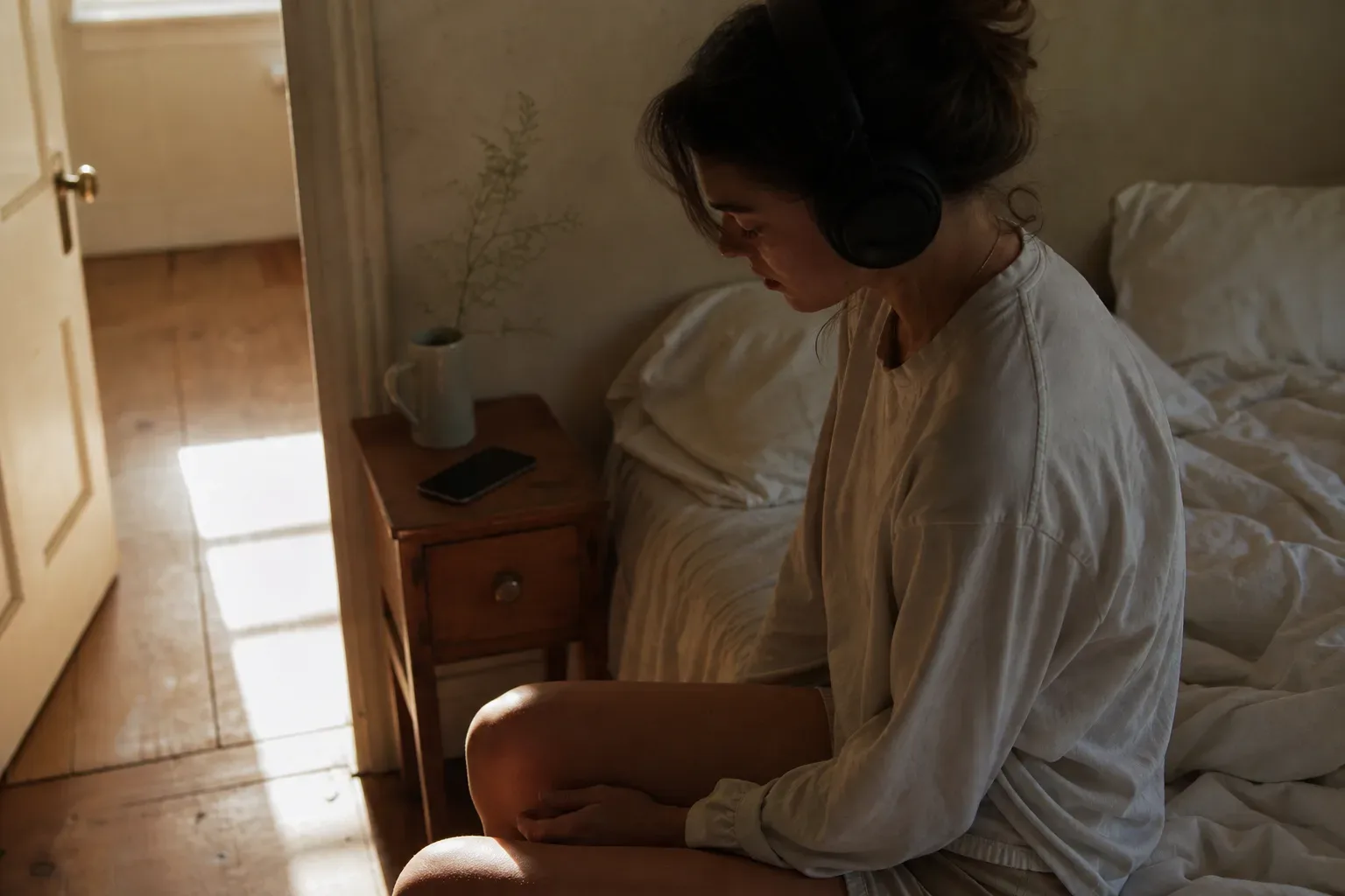 Woman listening to audio beside a dim bedroom window