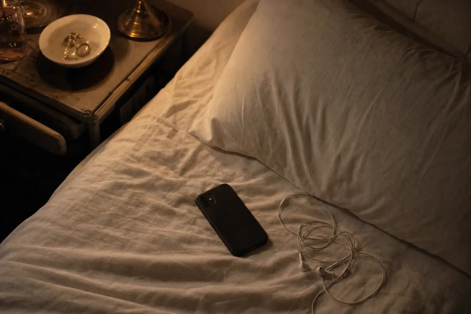 Phone beside a bed with headphones at night