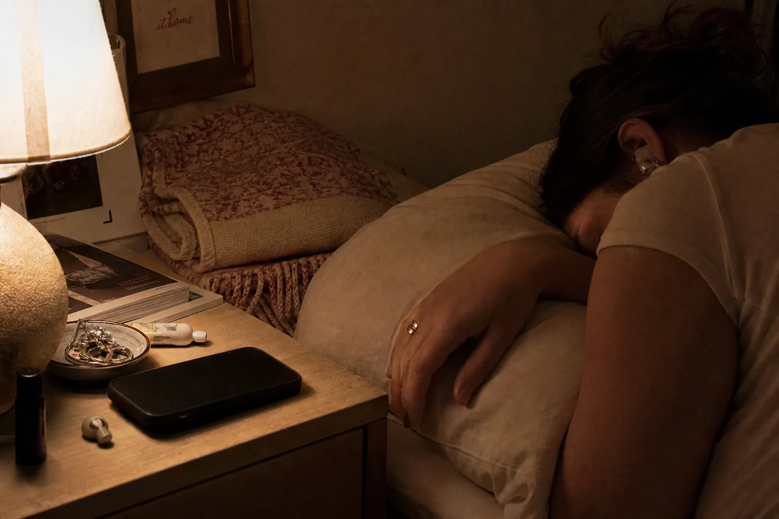 Person listening to audio beside a dim bedside lamp